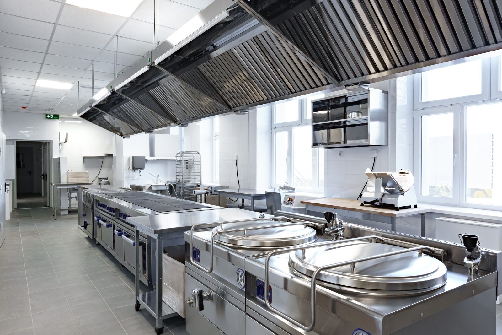 A stainless steel commercial kitchen with extraction canopies over the cooking line