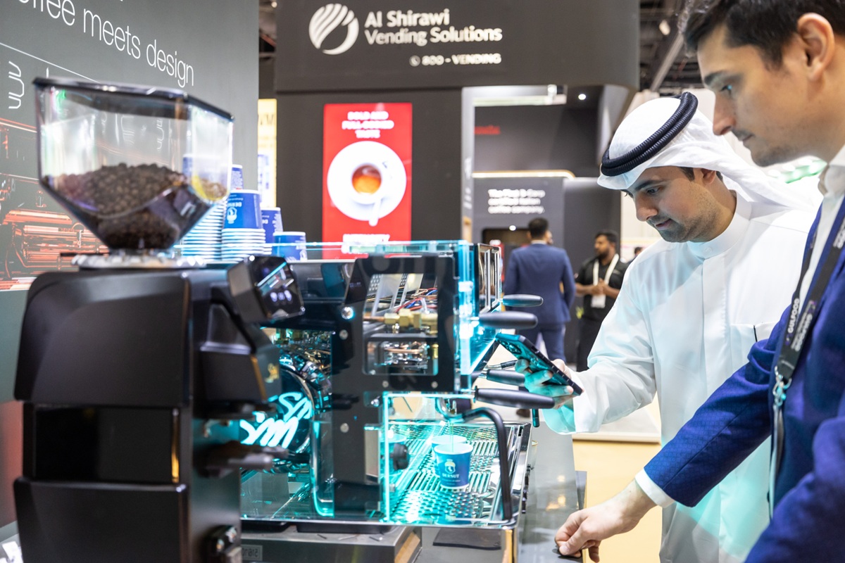 Visitors inspecting an illuminated commercial espresso machine and grinder at GulfHost