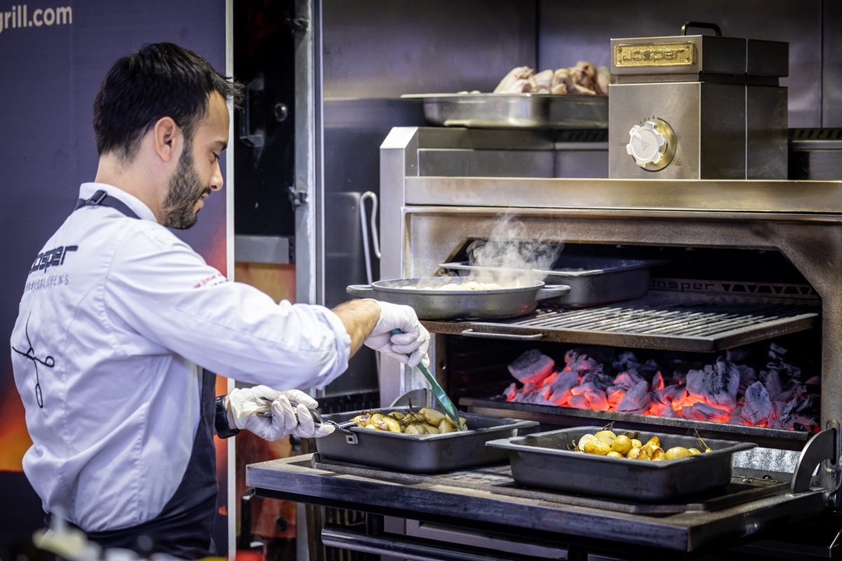 A chef cooking over charcoal in a commercial grill oven during a GulfHost demonstration