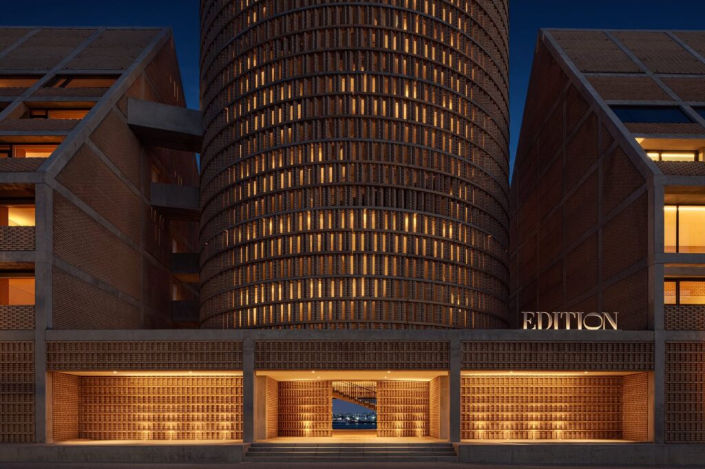 The hotel's entrance at dusk, a lit brick cylinder rising behind the EDITION sign
