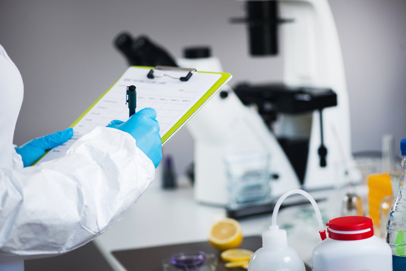 A laboratory technician recording results on a clipboard beside test equipment.