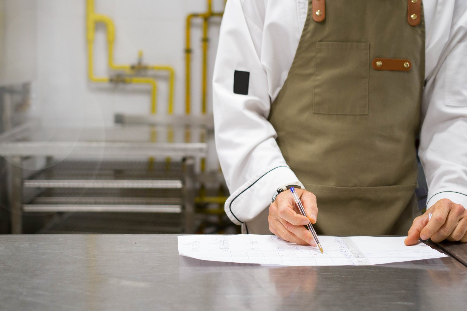 A chef filling in a checklist on a stainless steel counter.