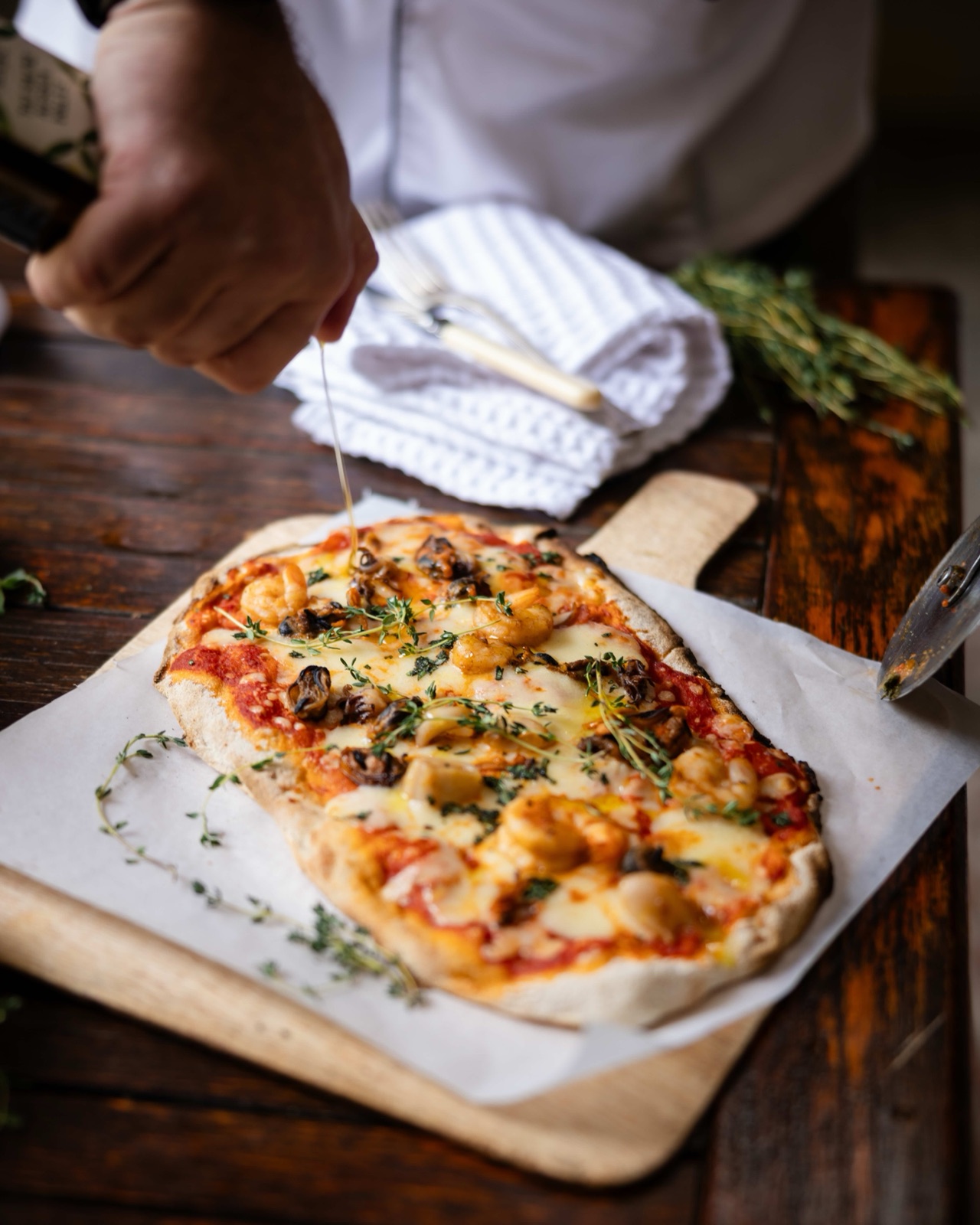 A server sets down a pinsa topped with cheese, tomato and herbs on a wooden board