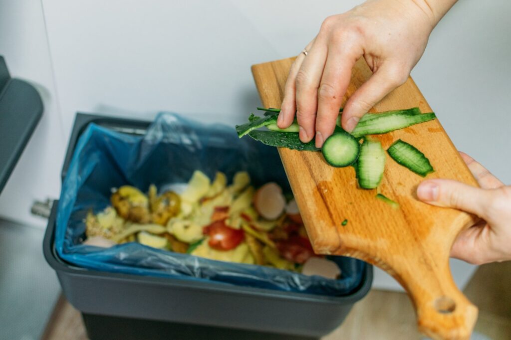 Vegetable offcuts scraped from a wooden board into a lined kitchen bin