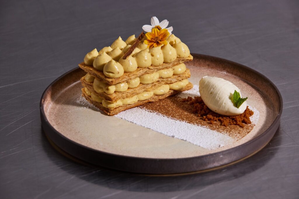 Mille-feuille piped with cream, with a quenelle and a crumb on a dark plate