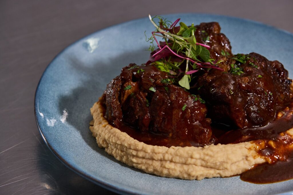 Braised meat in a glossy sauce on a smooth purée, topped with micro herbs
