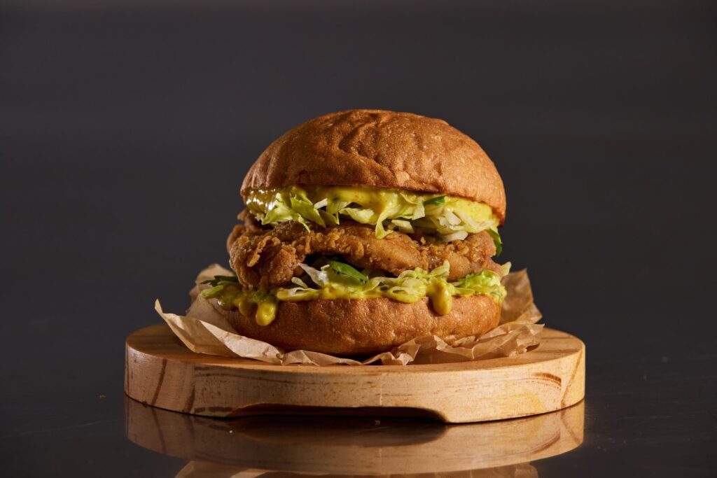 A fried chicken burger with slaw on a wooden board